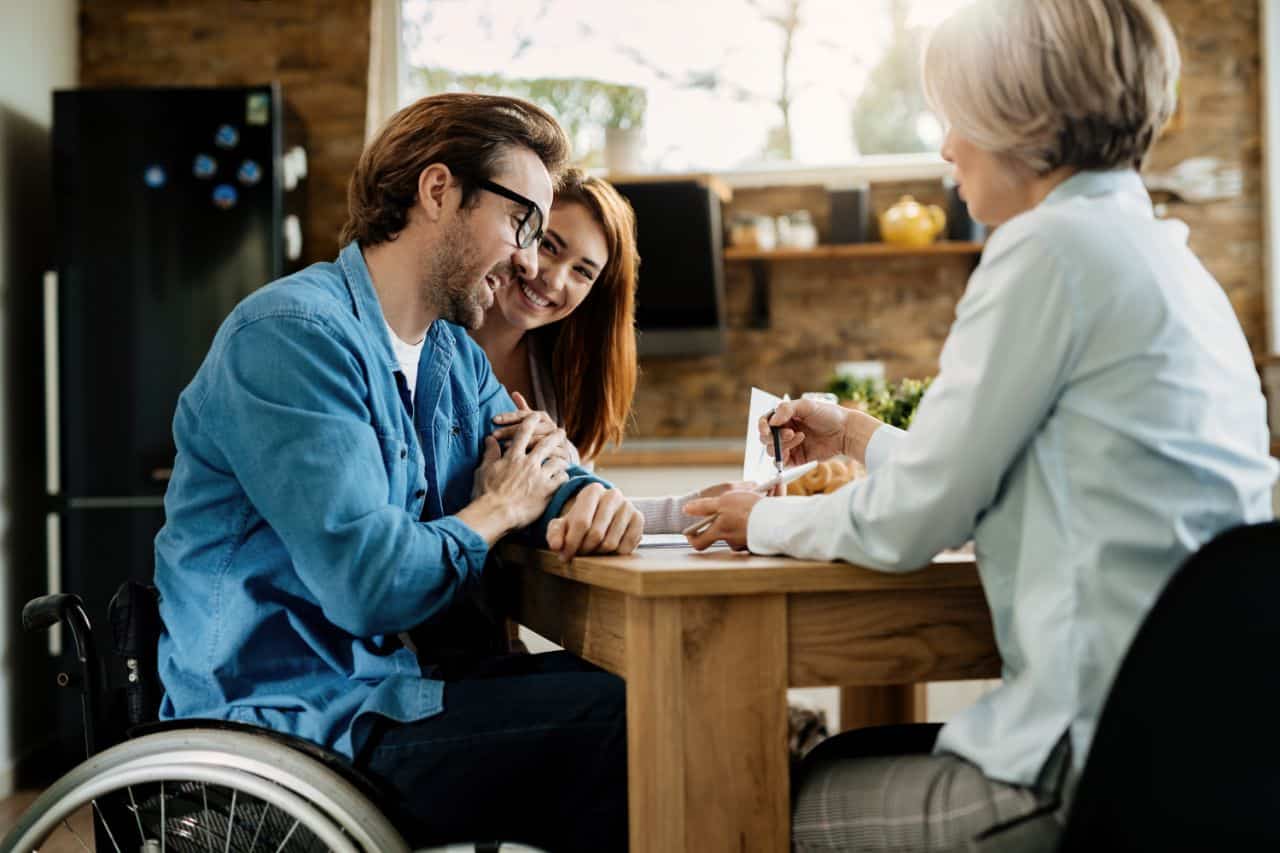 A young couple with the man in wheel chair consulting with a social worker. 